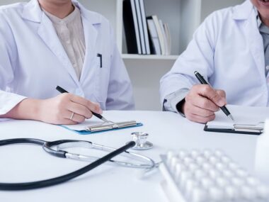 Nucala | ANCA Vasculitis News | Treatments | Two people in lab coats write on clipboards in office setting