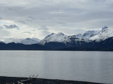 Snow-covered mountains jut up on the opposite side of a bay. The sky appears dark and stormy.