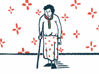 An elderly woman is seen walking with the assistance of a cane in a wallpapered room.